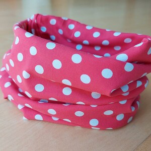 Könnte beinhalten: Ein rosa Stoff-Halswärmer mit weißen Punkten.