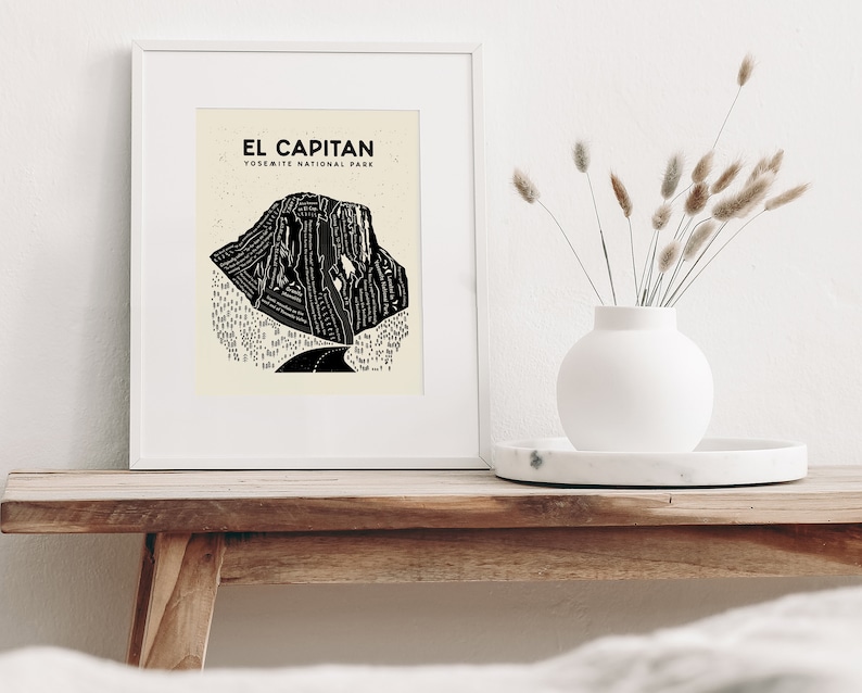 May include: A framed black and white illustration of El Capitan in Yosemite National Park. The illustration is a stylized depiction of the rock formation with a road winding through the base.
