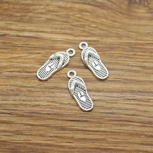 May include: Three silver-toned flip-flop charms with a textured design. The charms have a loop at the top for attaching to jewelry or other crafts.