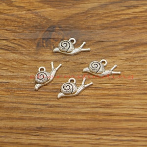 Peut inclure: Quatre breloques d'escargots en argent avec des motifs de coquille détaillés. Les breloques sont parfaites pour la fabrication de bijoux, le scrapbooking et d'autres projets d'artisanat.