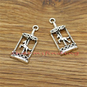 Puede incluir: Dos colgantes de plata con forma de carrusel con un caballo encima. Los colgantes son detallados y tienen un aspecto vintage.