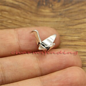 May include: Silver origami crane charm. The crane is a symbol of peace and good luck in Japanese culture.