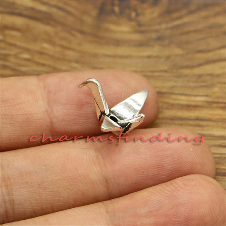 May include: Silver origami crane charm. The crane is a symbol of peace and good luck in Japanese culture.