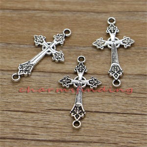 May include: Three silver-toned cross charms with ornate details. Each cross has two loops for attaching to jewellery or other crafts.
