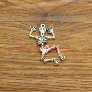 May include: Silver skeleton charm with a distressed finish. The skeleton is in a screaming pose with its arms raised and legs bent. The charm has a loop at the top for attaching to a necklace or bracelet.