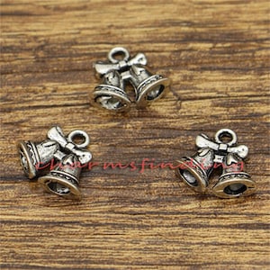 May include: Three silver-toned metal charms shaped like two bells tied together with a bow. The charms are ideal for adding a festive touch to jewellery or crafts.