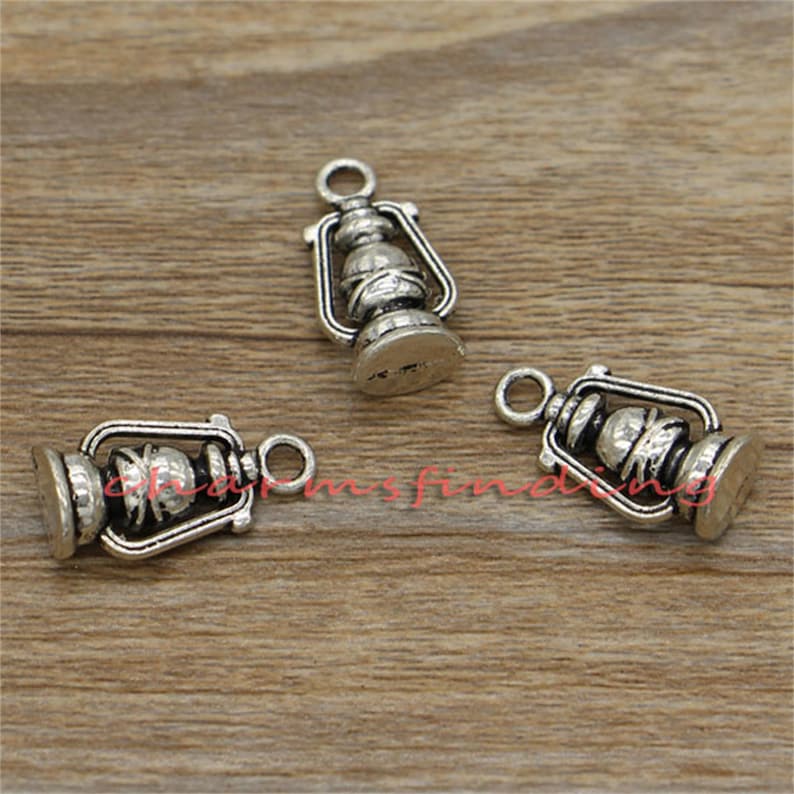 May include: Three silver-toned metal charms shaped like antique oil lamps. Each charm has a loop at the top for attaching to a necklace or bracelet.