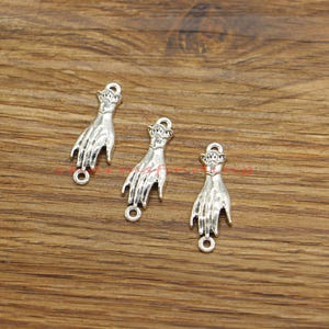 Puede incluir: Tres colgantes de plata con forma de mano con el dedo anular extendido. Los colgantes tienen un bucle en la parte superior para sujetarlos a una pulsera o collar.