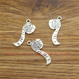May include: Three silver-colored tape measure charms with a spiral design on the top and measurement markings. Each charm has a small loop for attaching to jewelry or other crafts. The charms are made of metal.