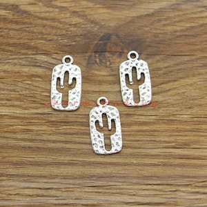 May include: Three silver-toned metal charms shaped like a cactus with a textured surface. The charms have a loop at the top for attaching to jewelry or other crafts.