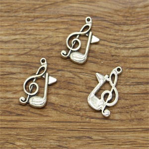 Könnte beinhalten: Drei silberfarbene Treble-Clef-Anhänger. Jeder Anhänger zeigt ein detailliertes Design eines Treble-Clefs mit einer Musiknote.
