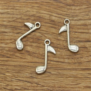 Könnte beinhalten: Drei silberne Musiknoten-Anhänger mit einer Schlaufe zum Anbringen an einer Halskette oder einem Armband.