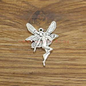 Puede incluir: Encanto de plata con un hada con las alas extendidas. El hada está representada en una pose de vuelo con un diseño delicado y detallado.