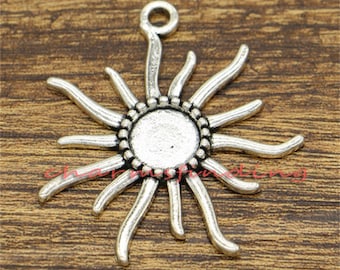 May include: A silver-toned metal sun pendant featuring a central circular bezel setting surrounded by a beaded border and twelve radiating wavy rays. The charm includes a small loop at the top for attachment and has the text charmsfinding printed across it.