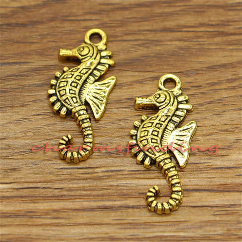 May include: Two gold-toned seahorse charms with intricate details. The charms have a textured surface and are perfect for jewelry making or crafting projects.