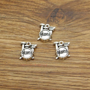 May include: Three silver-toned metal charms shaped like drum sets. Each charm features a drum with a musical note design and a small cymbal.