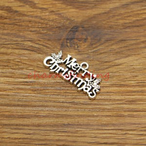 Könnte beinhalten: Silberner Anhänger mit den Worten "Frohe Weihnachten" und  Mistelzweigen.