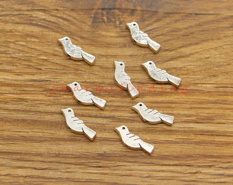 May include: Small, silver-colored bird charms with a distressed finish. Each charm features a simple bird silhouette with etched details and a small black dot for the eye. The charms are scattered on a wooden surface.