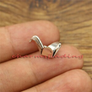May include: Silver origami crane charm pendant. The crane is folded in a traditional style and has a delicate, detailed design.