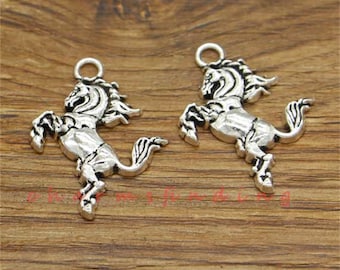 May include: Two silver-colored horse charms with a detailed design. Each charm features a rearing horse with a flowing mane and tail, and a small loop at the top for attaching to jewelry or other crafts. The charms are displayed on a wooden surface.