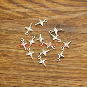 May include: A collection of silver-toned star-shaped charms with jump rings. The charms are scattered on a wooden surface.