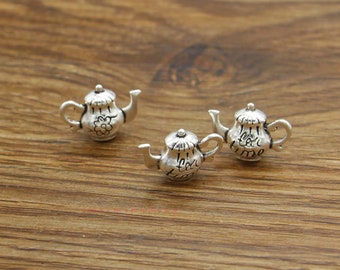 May include: Three silver teapot charms with the words "tea time" engraved on two of them. The charms are on a wooden surface.