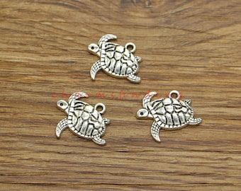 May include: Three silver-toned turtle charms with a detailed shell design. The charms have a loop at the top for attaching to jewelry or other crafts.