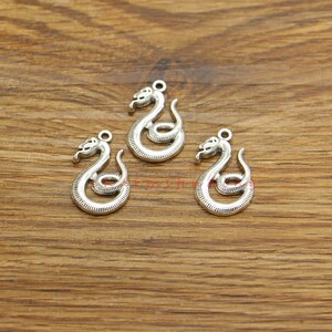 Puede incluir: Tres encantos de serpiente plateados con un diseño en espiral. Los encantos tienen una cabeza y una cola de serpiente detalladas.