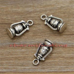 May include: Three silver-toned metal charms shaped like antique oil lamps. Each charm has a loop at the top for attaching to a necklace or bracelet.