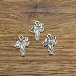 Op de afbeelding: Drie zilverkleurige metalen bedels in de vorm van een fakkel met een vlam aan de bovenkant. De bedels hebben een lus aan de bovenkant om aan een ketting of armband te bevestigen.