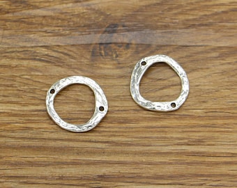 May include: Two silver-toned metal rings with a textured surface and three holes each. The rings are on a wooden surface.