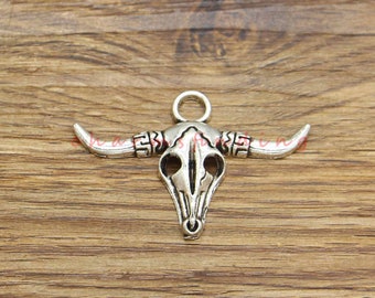 May include: Silver-toned bull skull pendant with curved horns and a loop for hanging. The pendant has detailed features and a rustic, Western-inspired design. The skull measures approximately 2 inches wide.