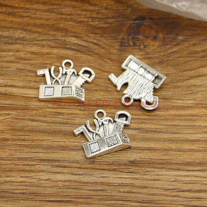 May include: Three silver-toned metal charms shaped like toolboxes with various tools inside. The charms have a vintage look and are perfect for adding a unique touch to jewelry or crafts.
