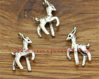 May include: Three silver-toned deer charms, each with a different pose, are shown on a wooden surface. The charms are detailed and have a vintage look.