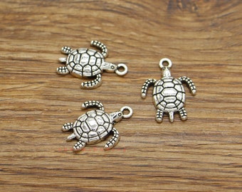 May include: Three silver turtle charms with a detailed shell design. The charms have a loop at the top for attaching to jewelry or other crafts.