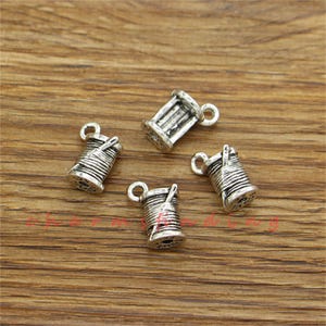 Pu&ograve; includere: Quattro ciondoli in metallo color argento a forma di rocchetti di filo con un ago. I ciondoli hanno un anello nella parte superiore per essere attaccati a una collana o un braccialetto.