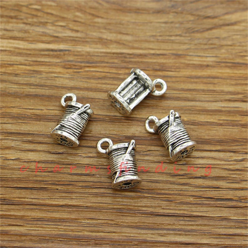 Pu&ograve; includere: Quattro ciondoli in metallo color argento a forma di rocchetti di filo con un ago. I ciondoli hanno un anello nella parte superiore per essere attaccati a una collana o un braccialetto.
