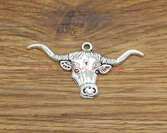 May include: Silver-toned metal charm in the shape of a bull's head with horns. The charm has a detailed design and is suitable for jewelry making.