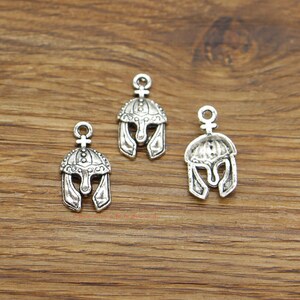 May include: Three silver-toned metal charms in the shape of a Roman helmet. Each charm has a loop at the top for attaching to a necklace or bracelet.