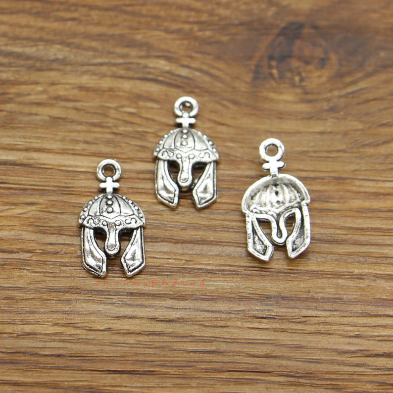 May include: Three silver-toned metal charms in the shape of a Roman helmet. Each charm has a loop at the top for attaching to a necklace or bracelet.
