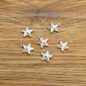 Może przedstawiać: Sześć srebrnych zawieszek w kształcie gwiazdy z pętelką do mocowania do biżuterii lub innych prac rękodzielniczych.