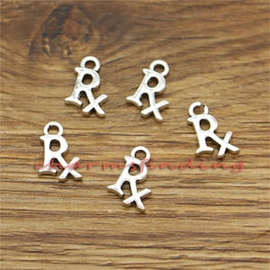 May include: Five silver charm pendants shaped like the letter "R" with a cross through it. The charms are on a wooden surface.