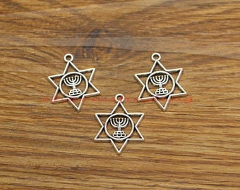 May include: Three silver-toned metal charms in the shape of a six-pointed star with a menorah inside a circle. The charms are on a wooden surface.