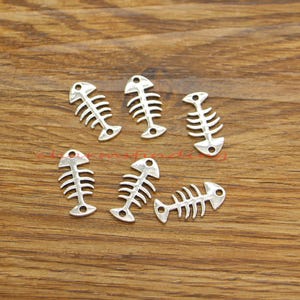 May include: Six silver fish bone charms, each with a different design. The charms are small and delicate, perfect for adding a touch of whimsy to jewellery or crafts.