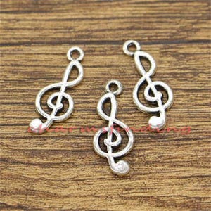 May include: Three silver treble clef charms, each with a different orientation. The charms are on a wooden surface.
