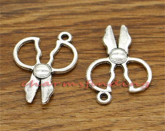 May include: Two silver-toned metal charms shaped like scissors. The charms have a loop at the top for attaching to a necklace or bracelet.