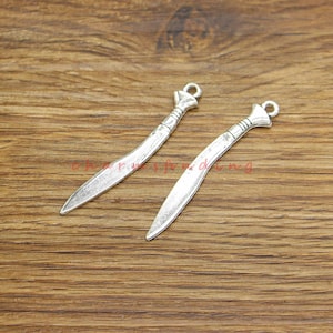 May include: Two silver-toned sword charms with a loop at the top for attaching to jewelry or crafts.