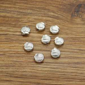 May include: Eight silver-toned metal seashell charms with a detailed design. The charms have two holes for attaching to jewellery or other crafts.