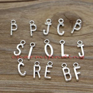 26 letras del alfabeto de la A a la Z. Dije con inicial de letra para collar o pulsera. Tono plateado antiguo. 6 x 16 mm. cf0057