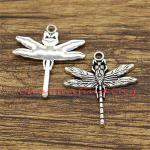May include: Two silver dragonfly charms with intricate details. The charms have a loop at the top for attaching to jewelry or other crafts.